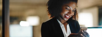 A photo of a young professional looking at her phone with a smile on her face. 